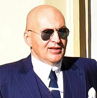 Lou Fanánek Hagen wearing a blue pin-striped suit and sunglasses, looking left of camera
