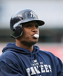 Robinson Canó, in a Yankees batting helmet and sweatshirt, blows a bubble gum bubble.