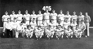 A black and white photograph of baseball players in uniforms and caps posed in three rows standing, sitting, and kneeing on a baseball field