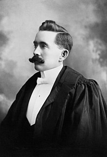 A formal portrait of a left-facing man with a moustache, wearing barrister's robes