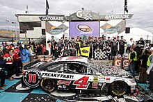 a parked race car covered with confetti and surrounded by celebrating team members