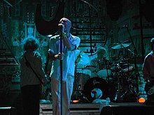 A color photograph of the band R.E.M. on stage