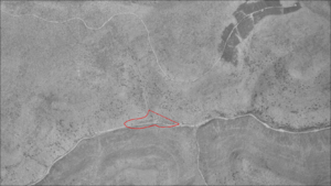 一条深溪谷的鸟瞰图，道路从左至右延伸，更小的山谷从顶部和底部连接起来。中间有一个大致呈三角形的红色形状。