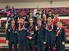 Group of students in dark blue jumpsuits holding a trophy