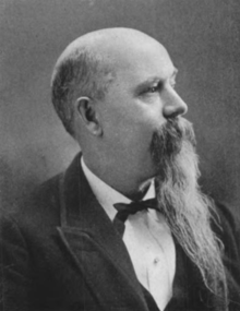 A black and white photograph of a man in a suit with a long beard