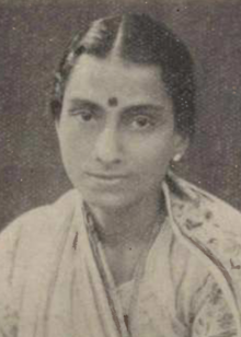 A young South Asian woman, dark hair parted center and dressed back to nape; wearing a light-colored sari