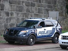A marked PAPD Ford Police Interceptor Utility patrol vehicle, parked on a sidewalk and occupied by a solo officer.
