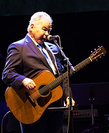 Prine onstage with a guitar and a microphone