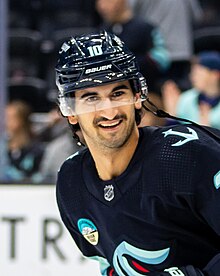 Hockey player smiling with his neck turned while wearing a blue Seattle Kraken hockey jersey