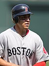 A young man in a grey baseball jersey wearing a batting helmet with eyeblack under his eyes.