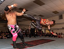 Arquette in mid-air, sending wrestler Ethan Page reeling