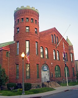 A brick building with a castle-type tower on the left and a smaller tower with green roof on the right