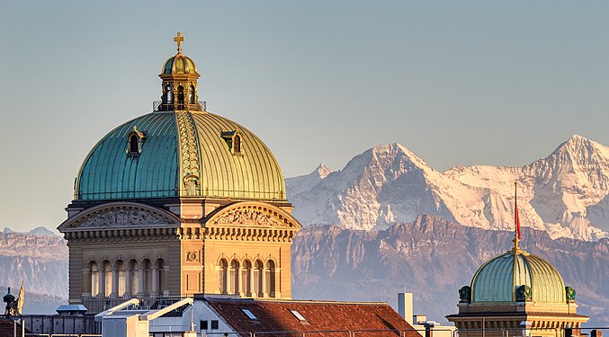 Federal Palace in Bern. Central and western domes in evening light with the peaks of Eiger and Mönch in the background.