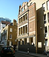 Facade of the former Cock & Hoop public house, Spitalfields, London, preserved as part of Lilian Knowles House (student accommodation for the London School of Economics), constructed 2005. The facade stands clear of the new building, attached by pins; the floor levels and fenestration of the two buildings are unrelated.