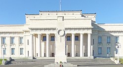 The face of a neoclassical building in Auckland, New Zealand, with a cenotaph (a type of war memorial) in front.