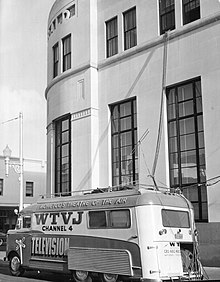 A converted bus is parked outside the Miami Herald offices, cables run from a second story to inside the van. The van is emblazoned with the legends "Wometco's Theatre of the Air", "WTVJ Channel 4 Television", "Stop Look Listen", and partially visible is one listing network affiliations including CBS, ABC, and NBC (not visible: DuMont)