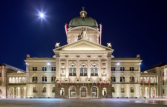 Federal Palace of Switzerland (Bundeshaus) – Pediment with inscription Curia Confoederationis Helveticae (assembly of the Swiss federation) – view including the allegorical sculpture of executive, independence, and legislative as well as the central dome crowned by the swiss cross – pictured during full moon with clear night sky.