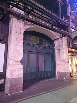 The former entrance to the Liberty Theatre on 42nd Street. It consists of a set of green doors within a stone archway. There is an electronic sign above the door.