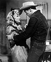 梦露和唐·默里于《巴士站》。她穿着一件破旧的外套和一顶用绳扎的小礼帽，正与身着牛仔裤、牛仔夹克和牛仔帽的默里争吵。