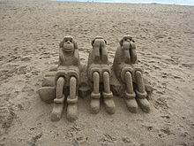 Photograph of the three wise monkeys sculpted out of sand on a beach