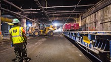 Workers constructing the station's upper concourse, which is located within part of the Grand Central Terminal's Madison Yard. There is construction equipment being stored alongside the walls of the yard.
