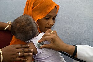 a mother holds a baby while a doctor places a stethoscope on their back