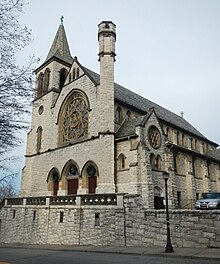 Upward view from street level of a church building with a white and brown marble facade in the Gothic Revival style on a cloudy day