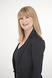Free publicity photo: waist high portrait in profile of middle aged woman with long blond hair and bangs wearing a black jacket