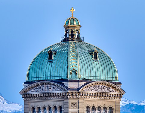 Federal Palace in Bern. Central dome crowned by the Swiss Cross in evening light against the background of the Bernese Alps.