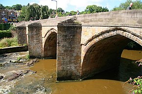 Close up of natural stone arched bridge and tapered piers over river on a sunny day with blue sky