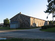 A one story building with a slanted roof, sitting next to a road and driveway.