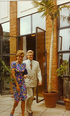Princess Diana where a flower patterned dress walking beside London Lighthouse director Christopher Spence, who is wearing a cream double-breasted suit.