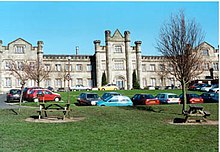 A scene of a castle-like school, with cars and a parking lot in front of it.
