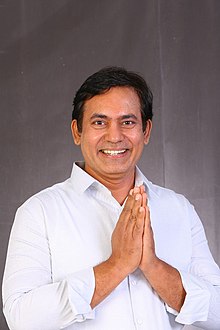 head-and-shoulders image of a dark-haired man smiling, with hands clasped as if in prayer