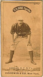 A baseball player standing facing the camera with his hands resting on his knees