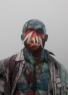 Upper body and head of François Sagat, with blue skin, blood on his chest and face, and teeth protruding from his eyes and nose