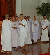 Nine Asian women dressed in white robes are standing and talking. Eight are shaven, one is not.