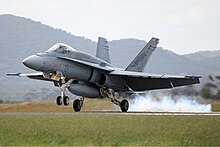 Photo of a modern fighter aircraft landing on a runway. Mountains are visible in the background of the photo.