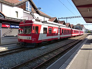 Red-and-white train on double-tracked railway line in front of station building