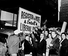 A cheering group of people point to a campaign banner