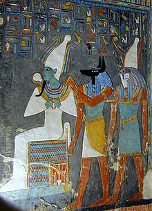 Painted relief of a seated man with green skin and tight garments, a man with the head head of a jackal, and a man with the head of a falcon