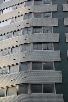 Detail of the facade, which contains a color palette of dark-green mosaic tile and turquoise brick, interspersed with windows