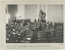 Parliament is convening for the first time after the war. White and German soldiers dominate the picture while only one person from the opposition social democrats is present. Thus, it was sarcastically called a Rump Parliament.