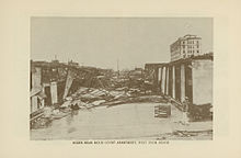 An image showing devastated apartment buildings, with debris blocking the road
