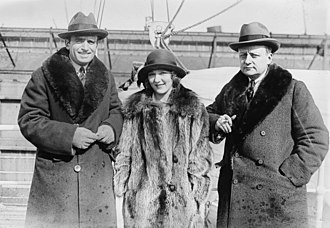 Three white people, man, woman, man wearing hats and thick coats on the deck of a ship