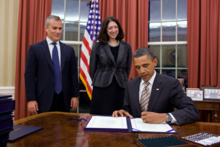 Image of Barack Obama signing the bill with Jeffrey Zients and Shelley Metzenbaum looking on.