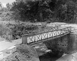 Photograph of the Hondo River Bridge, a narrow, one-lane, single-span bridge set on masonry abutments, over a small river
