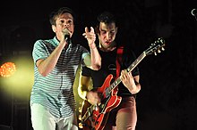 Two men; one singing into a microphone and the other playing guitar
