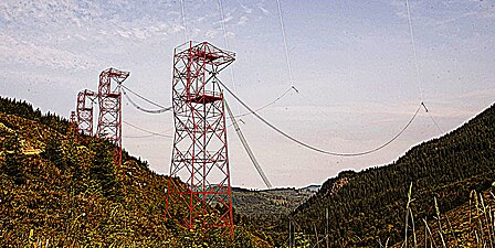 Towers supporting one of two antenna feed bus cables extending along the valley floor from the transmitter building. From each 145 feet (44 m). tower a vertical feedline (faintly visible, top of picture) extends up 900 feet (270 m). to attach to the midpoint of each horizontal valleyspan cable.