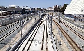 Six parallel tracks viewed from a bridge. The middle two tracks are in a concrete dive structure heading towards a tunnel